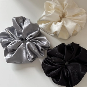 Three satin hair scrunchies in silver, cream, and black with embossed rose patterns