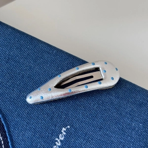 Gros plan d'une pince à cheveux en cuir argenté à pois bleu clair sur un fond denim