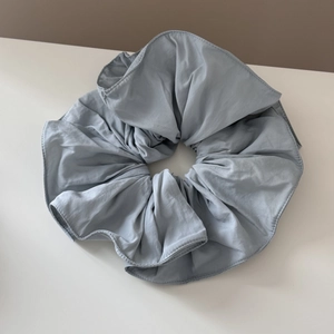 Close-up of light gray blue fabric scrunchie with detailed ruffled edges and soft texture