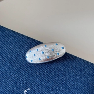 Vue macro d'une pince à cheveux argentée à pois bleus sur une texture de tissu denim