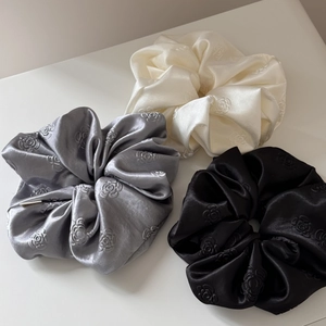 Close-up of three satin scrunchies in silver, cream, and black with rose floral embossing