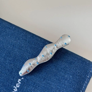 Détail d'une pince à cheveux argentée ondulée à pois bleus sur un fond en tissu denim