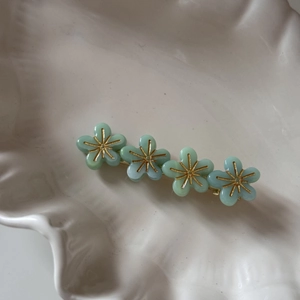 Gros plan de quatre pinces à cheveux fleurs vert menthe avec centres dorés sur plat