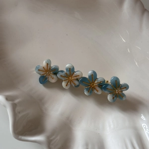 Gros plan de quatre fleurs en résine bleu et blanc sur pince dorée sur plateau blanc