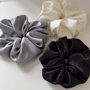 Detailed shot of satin scrunchies with embossed rose patterns in grey, cream, and black