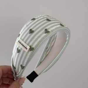 Detailed close-up of blue green striped headband with heart pattern and handmade label