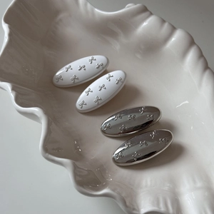 Set of four silver bow hair clips on a white ceramic shell tray in a minimalist style