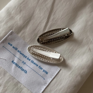 Detail view of silver embossed metal bow hair clips on a soft cream fabric background