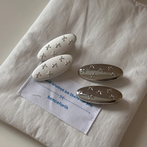 Detailed view of silver and cream oval hair clips with delicate 3D bow relief patterns