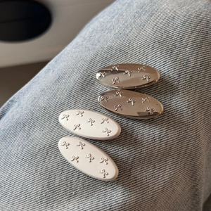 Set of four silver and white oval hair clips with embossed bow designs on denim