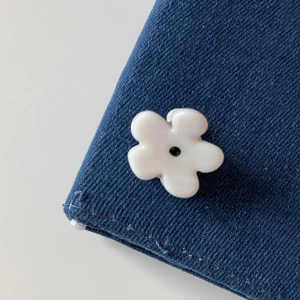 Close-up of a white flower hair clip with black bead center on denim fabric background