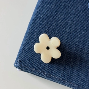 Detail of a minimalist cream floral hair clip with black center on denim fabric