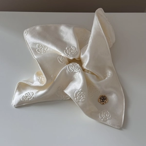 Detailed close-up of cream satin scrunchie with camellia texture and gold floral metal buckle