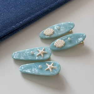 Detail of four blue acetate shell and starfish hair clips with pearls on denim background