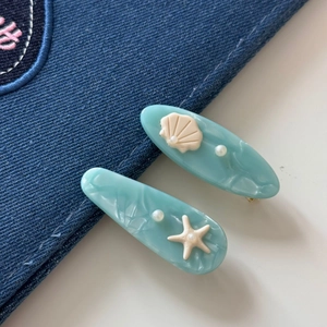 Blue seashell and starfish hair clips set in mint green resin on denim background