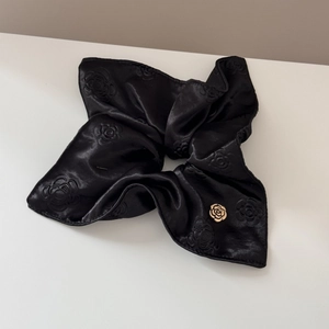 Detail of black satin hair scrunchie with camellia relief and golden metal flower buckle