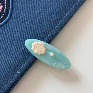 Close-up of light blue acetate hair clip with seashell relief and pearl on denim fabric