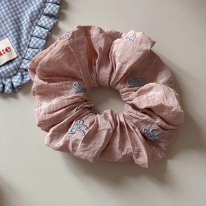 Vue rapprochée d'un chouchou rose en tissu plissé avec des motifs nœuds bleus brodés