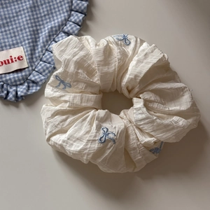 Texture détaillée du chouchou blanc cassé avec des motifs de nœuds brodés bleu clair