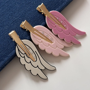 Close-up of three wing-shaped hair clips in white and pink colors with rhinestones