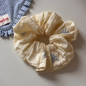 Détail du chouchou crème avec broderies de nœuds bleus et texture de tissu plissé