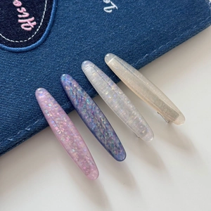 Detail of four oval hair clips with sparkling sequins on blue denim and white background