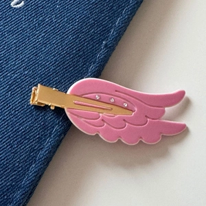 Close-up of pink wing-shaped hair clip with clear rhinestones on blue denim fabric