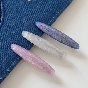 Detail of three colorful oval hair clips with glitter resin on blue denim fabric