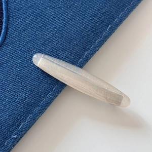 Macro shot of oval shell glitter hair clip on denim fabric showing translucent texture