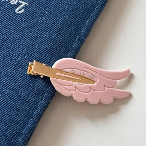 Close-up of pink wing hair clip with rhinestones and gold duckbill clip on denim fabric
