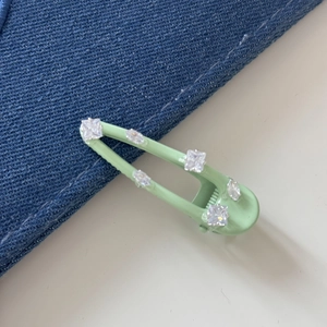 Detail van een lichtgroene haarspeld met kristallen op een denim stoffen achtergrond