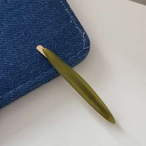 Detailed close-up of handmade olive green willow-leaf hair clip with gold logo lettering