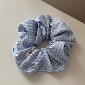 Detail of light blue striped scrunchie featuring delicate embroidery and woven brand label