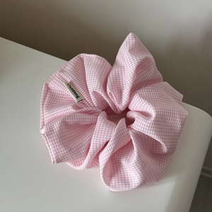 Close-up of pink plaid oversized fabric scrunchie with a brand label on white surface