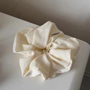 Close-up of cream-colored pleated scrunchie with subtle waffle texture and brand tag