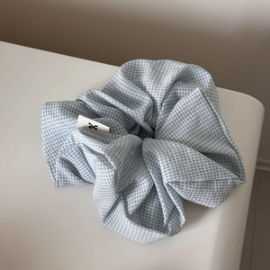 Close-up of light blue gingham hair scrunchie with soft fabric texture and side label