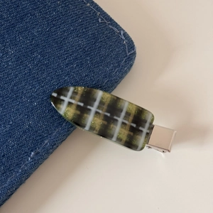 Détail d'une pince à cheveux à carreaux vert et blanc sur denim avec clip métallique