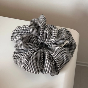 Close-up of a premium black and white gingham scrunchie with soft fabric texture and logo