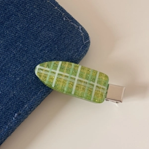 Détail d'une pince à cheveux à carreaux verts avec résine pailletée sur tissu denim