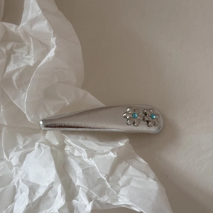 Dettaglio del fermaglio per capelli argento con fiori in strass blu su carta strutturata
