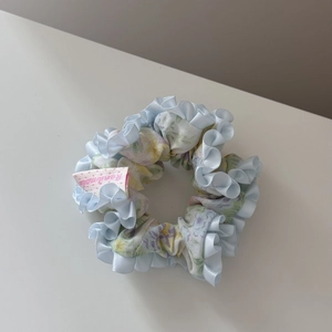 Détail d'un chouchou floral avec bord à volants en satin bleu clair et étiquette handmade