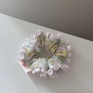 Vue macro d'un chouchou floral vert clair avec bords à volants en satin rose et petite étiquette