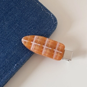 Détail d'une pince à cheveux à carreaux orange avec paillettes dorées et clip argenté