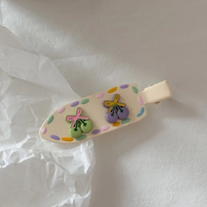 Dettaglio del fermaglio per capelli a ciliegia color crema con pois su sfondo bianco