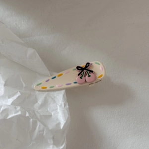 Dettaglio del fermaglio per capelli a ciliegia crema con pois colorati e fiocco