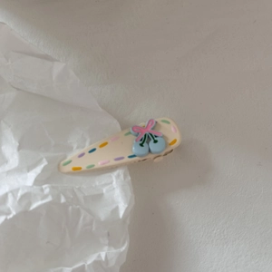 Dettaglio della molletta color crema con pois colorati, ciliegie blu e fiocco rosa