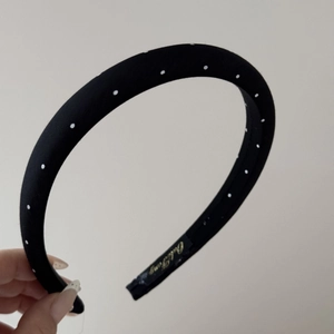Detailed close-up of a black fabric headband with white polka dots and gold label