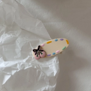 Dettaglio del fermaglio crema con ciliegie rosa, pois colorati e fiocco nero