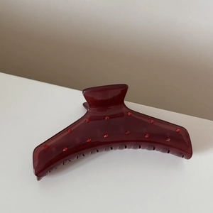Détail d'une pince à cheveux en acrylique bordeaux avec strass rouges et dents serrées