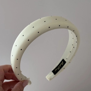 Detail of padded headband with black polka dot print and brand label on grey background